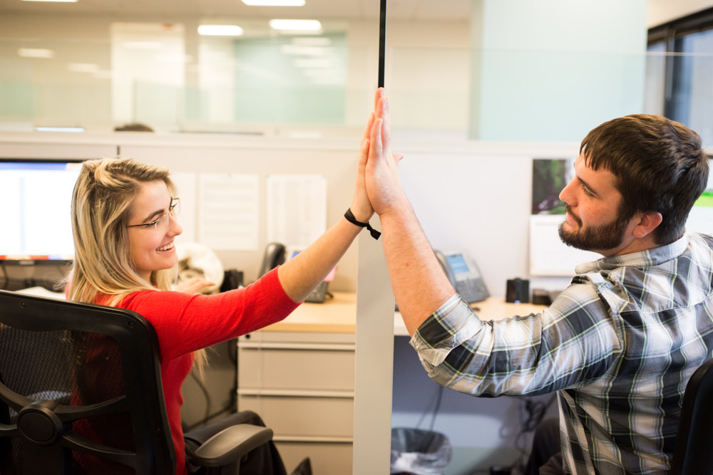 Two workers high five between their desks